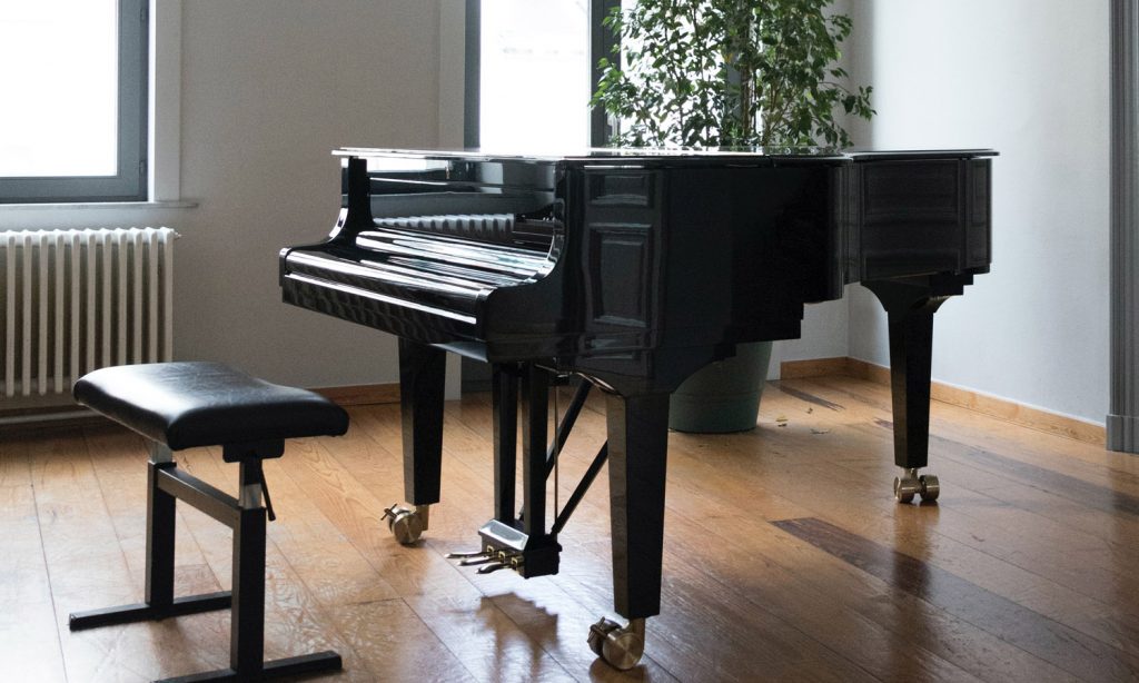 grand piano with a closed lid standing in a room with wooden floors and white walls
